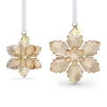 Two faceted snowflake ornaments in a pale champagne-gold tone, shown hanging against a white background. One ornament is turned to show the side with a white hanging ribbon and a small gold tag engraved with '2028'; the other is shown from the front.