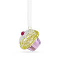 A cupcake-shaped hanging ornament with a faceted yellow frosting top, clear rhinestone-like crystals, a small red gem, and a lavender-purple base, suspended from a white ribbon on a white background.