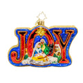 A Christopher Radko glass ornament with a nativity scene featuring figures of Mary, Joseph, and baby Jesus, and the word 'JOY' in bold letters. The background is blue with a golden 'S' shaped star at the top.