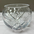 A clear cut-crystal tumbler with a faceted geometric pattern, resting on a white surface against a neutral gray background.